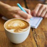 kopje cappuccino en vrouw die in dagboekje schrijft