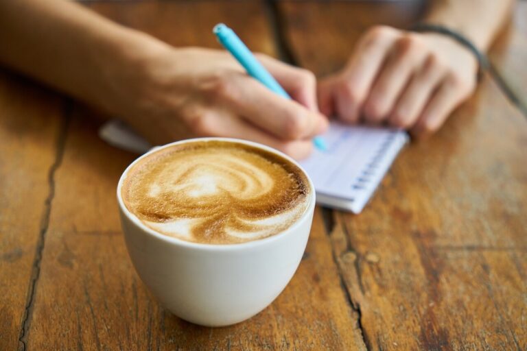 kopje cappuccino en vrouw die in dagboekje schrijft