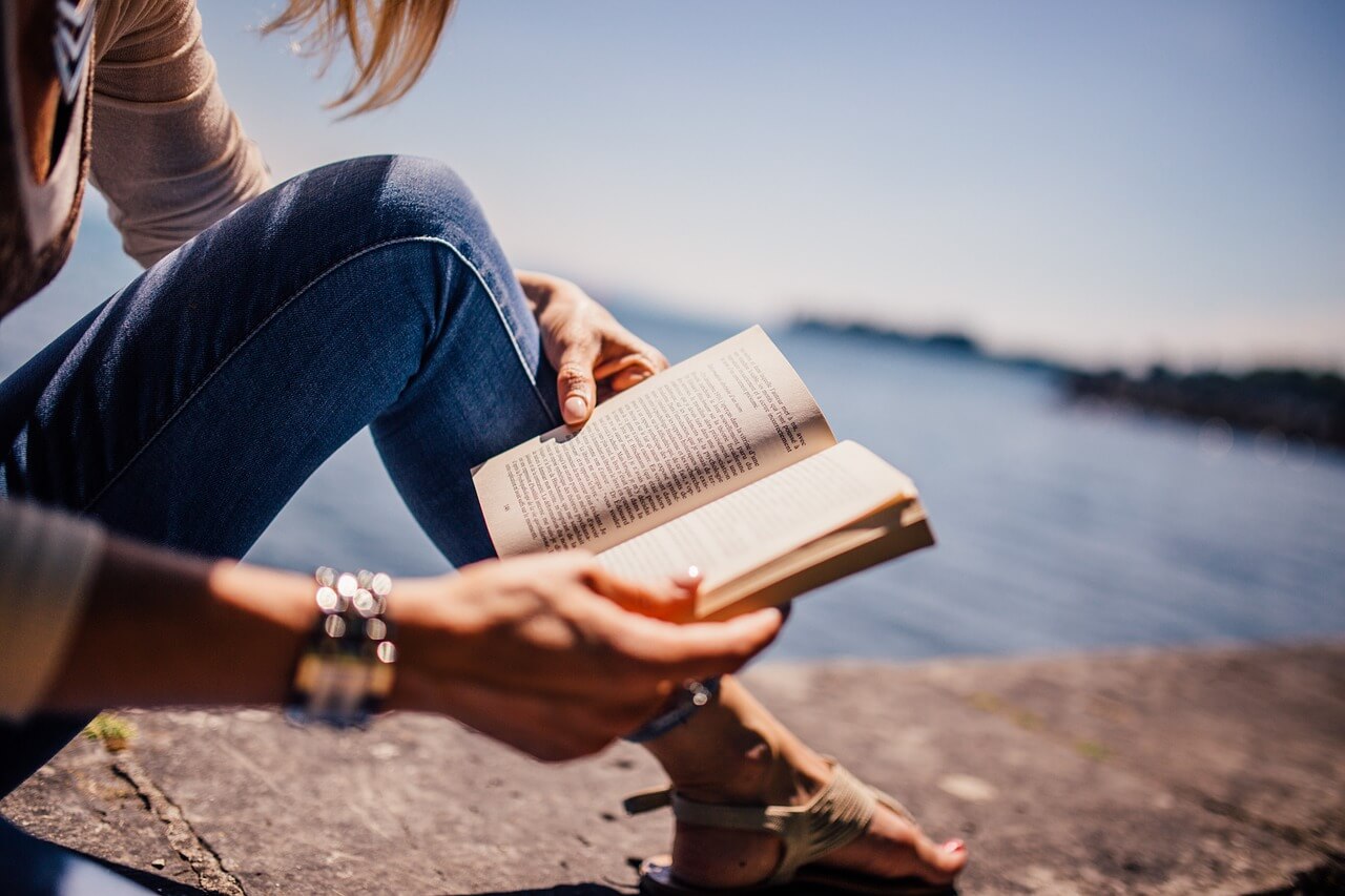 man leest boek op een stijger naast het water